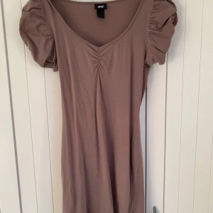 Beige klänning  - Säljer en beige/brun klänning från H&M. Man får jättefin figur i klänningen och den är gjord av mjukt tyg som inte nopprar. Syns dåligt på bilden men klänningen är ganska kort och slutar typ mitt på låret🫶