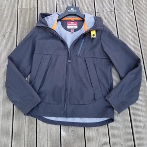 Svart jacka från Parajumpers - Säljer en stilren svart windbreaker från Parajumpers med huva och dragkedja. Jackan har en orange detalj vid halsen och en bröstficka med dragkedja. Perfekt för vår och höst då den är bra när det blåser mycket men man kan även ha den på kallare sommarkvällar. Den passar bäst om du är 155 men passar fotfarandebra på mig som är 172| MVH Sam