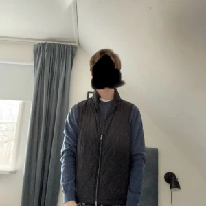 Svart quiltad väst från Oscar Jacobson - Snygg svart quiltad väst från Oscar Jacobson med dragkedja framtill. Perfekt för lager-på-lager stil. Västen har en stilren design och är lätt att matcha med olika outfits.