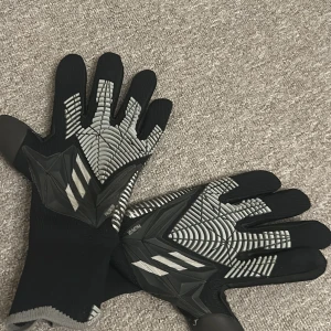 Svarta fotbollshandskar från Adidas - Snygga svarta fotbollshandskar från Adidas med grå detaljer och greppvänlig yta. Perfekta för att förbättra ditt spel på planen. De har en modern design med elastiska muddar för en säker passform. Köpte de för 599 och säljer de för 199