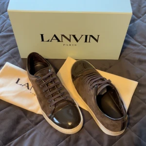 Bruna sneakers från Lanvin - Snygga bruna sneakers från Lanvin med en kombination av mocka och skinn. Skorna har en rund tå och snörning framtill. Perfekta för en stilren look.