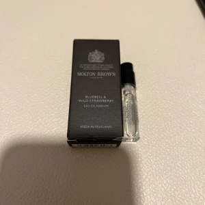 Molton Brown Bluebell & Wild Strawberry Eau de Parfum - Upptäck en elegant doft från Molton Brown med noter av blåklocka och vild jordgubbe. Denna Eau de Parfum kommer i en stilren svart förpackning och en liten glasflaska på 1,5 ml. Perfekt för att prova en ny doft eller ha med på resan.
