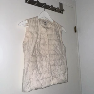 Vit quiltad dunväst Uniqlo - Säljer en stilren vit quiltad dunväst från H&M. Perfekt för lager-på-lager under kyliga dagar. Västen har en enkel design utan krage och stängs med knappar framtill.