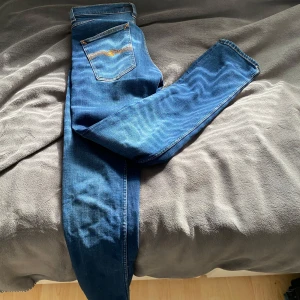 Blåa jeans från Nudie  - Säljer ett par snygga blåa jeans från Nudie.  Märkeslogga på bakfickan och knappar baktill. Använda ett par gånger men i mycket bra skick. Storlek 31/32, modellen är Grim Tim! Hör av dig vid fler frågor eller bilder!