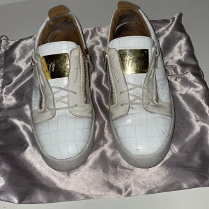 Vita giuzeppe zanotti - Snygga vita giuzeppe Zanotti  med krokodilmönster och gulddetaljer. Skorna har snörning och dragkedja på sidorna för en unik look. Perfekta för att ge din outfit en lyxig touch. Lite skador ifrån användning skulle säga skick runt 6-7/10 konkta vid minsta fråga. Dustbag ingår.