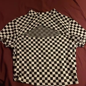 Svartvit rutig topp från FBSister - Snygg svartvit rutig topp från FBsister med korta ärmar och en cool öppen ryggdetalj. Perfekt för att sticka ut med ett klassiskt mönster och modern twist. 🖤