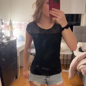 Svart topp med spetsdetaljer - Snygg svart topp med spetsdetaljer vid halsringningen. Toppen har korta ärmar och en tight passform🥰