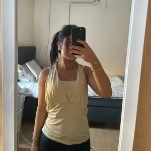 Beige halterneck topp - Säljer en snygg beige halterneck topp med djup urringning. Perfekt för varma sommardagar eller en utekväll. 90s stil topp
