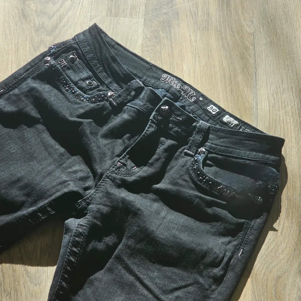 Snygga svarta jeansbyxor från Miss Me med dekorativa detaljer på bakfickorna. Byxorna har en normal passform och är prydda med glittriga stenar och broderier. Perfekta för att ge en extra touch till din outfit.. Farkut & Housut.