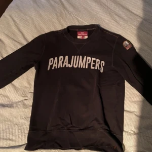 Svart fleece tröja från Parajumpers - Säljer en svart fleece tröja från Parajumpers med deras logga tryckt i vitt på framsidan. Tröjan har långa ärmar och en rund halsringning. Perfekt för kyliga dagar.