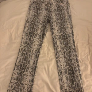 Ormmönstrade byxor från Guess - Snygga ormmönstrade byxor från Guess i svart och vitt. Byxorna har en normal passform och är perfekta för att ge din outfit en edgy touch. Tillverkade i ett bekvämt material som passar för olika tillfällen.