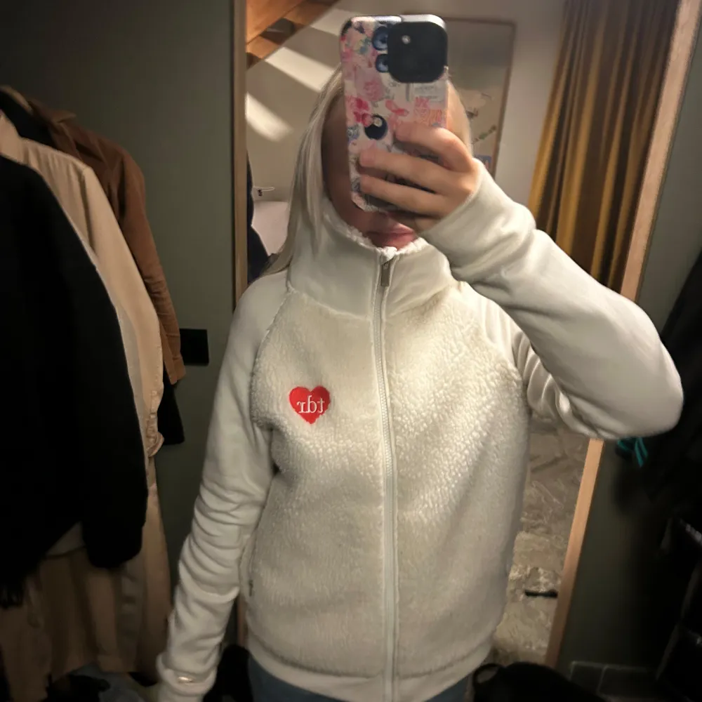 Säljer en mysig vit fleecejacka med dragkedja och en söt hjärtdetalj på bröstet. Jackan har långa ärmar och en hög krage som håller dig varm. Köpt i new York för 60$. Känner inte igen märket. . Takit.