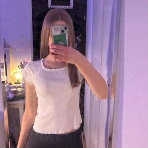 Vit ribbad topp - Säljer en stilren vit ribbad topp med korta ärmar. Toppen har en enkel och klassisk design som passar perfekt till vardags. Den är tillverkad i ett mjukt och bekvämt material.