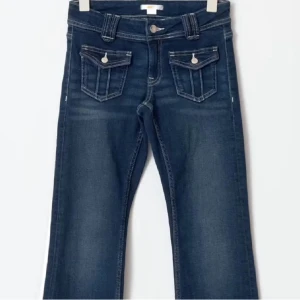 Mörkblå jeans med fickdetaljer - Snygga mörkblå jeans med unika fickdetaljer och knappar framtill. Perfekta för en avslappnad stil med en touch av karaktär. Passar bra till både sneakers och boots.