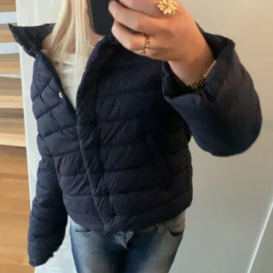 Marinblå quiltad dunjacka - Snygg svart quiltad dunjacka med dragkedja och knappar. Jackan har en normal passform och långa ärmar, perfekt för kyligare dagar. En stilren och praktisk jacka för höst och vinter, från gina tricot! 