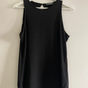 Svart ärmlös topp från KIOMI - Säljer en stilren svart ärmlös topp från KIOMI. Toppen har en rund halsringning och en liten öppning i ryggen som ger en snygg detalj. Perfekt för både vardag och festliga tillfällen. 🖤