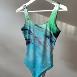 Turkos printad baddräkt - Turkos baddräkt med vatten-print. Den har breda axelband och en rund halsringning. Använd kort en gång till en plåtning - inte badat med den! 