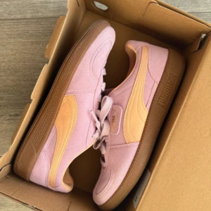 Rosa sneakers från Puma - Ett par assnygga rosa sneakers från Puma i modellen Palermo. Skorna är i ljusrosa med persikofärgad logga och en brun sula. Perfekta för vår och sommar, säljer eftersom de tyvärr var för stora 💞använda endast en gång 
