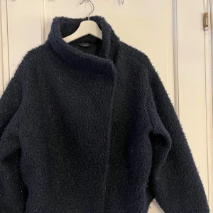 Mörkblå teddyjacka - Säljer en mysig mörkblå teddyjacka med hög krage. Jackan har en enkel och stilren design som passar perfekt för kyliga dagar. Den är långärmad och har en mjuk och fluffig textur.