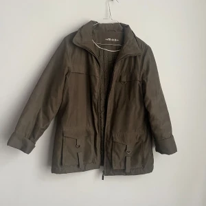 Vintage Olivgrön jacka från Mox - Säljer en olivgrön jacka från Mox med dragkedja och praktiska fickor framtill. Jackan har långa ärmar och en quiltad insida för extra värme. Perfekt för kyligare dagar.