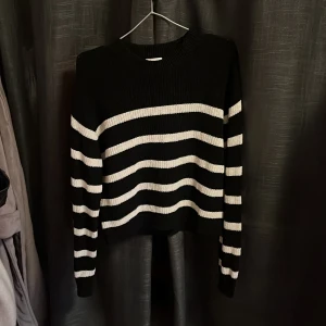 Svart och vit randig stickad tröja från H&M - Säljer en svart och vit randig stickad tröja från H&M. Tröjan har långa ärmar och en klassisk rund halsringning. Perfekt för en stilren och bekväm look.
