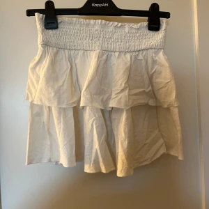 Vit kjol från Shein - Säljer en söt vit kjol från Shein med volangdetaljer. Kjolen har en elastisk midja för en bekväm passform. Perfekt för varma dagar!