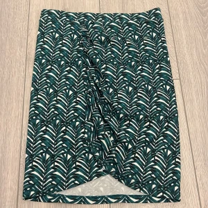 Mönstrad kjol i grönt och vitt - Snygg kjol med ett tropiskt mönster i grönt och vitt. Kjolen har en omlott-design som ger en fin detalj framtill. Perfekt för att ge en färgklick till din garderob!