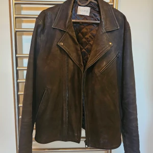 Brun skinnjacka från Denimes - Säljer en snygg brun skinnjacka från Denimes. Jackan har en klassisk design med dragkedja och flera fickor. Insidan är quiltad för extra komfort. Perfekt för en stilren look.