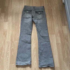 Grå bootcut jeans - Snygga grå bootcut jeans med klassisk femficksdesign och knappgylf. Perfekta för en avslappnad stil med en touch av retro. Passar bra till både sneakers och boots.