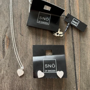 Halsband och örhängen från SNÖ of Sweden - Säljer ett set med halsband och örhängen från SNÖ of Sweden. Båda smyckena har hjärtformade hängen med glittriga detaljer. Perfekt för att lägga till lite extra bling till din outfit.