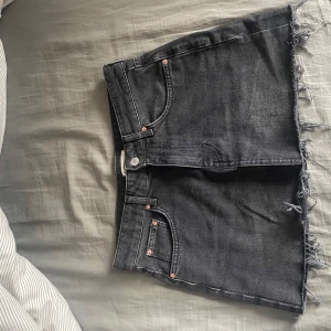 Svarta jeanskjol med fransar - Snygga svarta jeansshorts med fransiga kanter. Perfekta för en avslappnad stil. De har klassiska fem fickor och knappgylf.