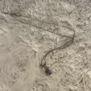 Silverfärgat halsband med lila kristall - Elegant silverfärgat halsband med en lila kristall som hänge. Perfekt för att lägga till en touch av färg och stil till din outfit.