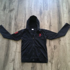 Navyblue  U.S. POLO ASSN - Snygg marinblå hoodie med dragkedja och röd broderad logga på bröstet och ärmen. Perfekt för en avslappnad stil. Den har en praktisk huva och långa ärmar.