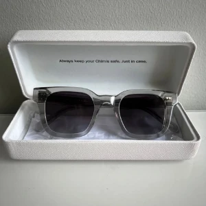 Chimi 04 - Snygga transparenta solglasögon från Chimi med fyrkantig form och mörka linser. Perfekta för en stilren look. Kommer i ett praktiskt fodral för säker förvaring.