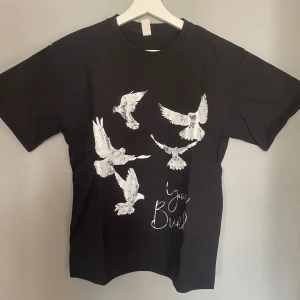 Svart t-shirt med fågeltryck - Snygg svart t-shirt med ett coolt tryck av vita fåglar i flykt. Perfekt för en avslappnad stil. T-shirten har en normal passform och korta ärmar.