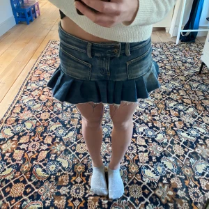 Jeanskjol med volang - Säljer en cool självsydd jeanskjol med volangdetaljer. Kjolen har en kort passform och är perfekt för en avslappnad stil. Den har klassiska jeansfickor och en knapp framtill. Perfekt för dig som vill ha en trendig look! Lite olika längd på volangen fram och bak men inget som märks tydligt!