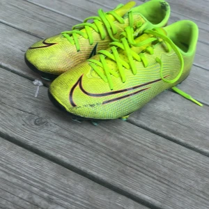 Neongula fotbollsskor från Nike - Säljer ett par neongula fotbollsskor från Nike med snörning och rund tå. Skorna har en iögonfallande design med svarta och röda detaljer. Perfekta för fotbollsplanen med sina dobbar för bra grepp.
