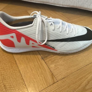 Nike Mercurial fotbollsskor - Säljer ett par Nike Mercurial fotbollsskor i vitt och rött med svart swoosh. Skorna har snörning och är designade för optimal prestanda på planen. Perfekta för den som vill ha stil och funktion i ett.