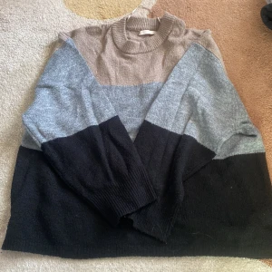 Randig stickad tröja från 157 - Säljer en mysig stickad tröja från 157 i storlek S. Tröjan har ett randigt mönster i svart, grått och beige med långa ärmar och en hög krage. Perfekt för kyliga dagar!