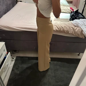 Beiga kostymbyxor med hög midja - Snygga beiga kostymbyxor med hög midja och raka, vida ben. Byxorna har knapp och dragkedja framtill och är perfekta för en stilren look. Skriv för mer info och bilder;))