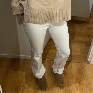 Vita bootcut byxor med dragkedja - Snygga vita bootcut byxor med dragkedja och hällor för bälte. Byxorna har en klassisk passform och är perfekta för en stilren look. Materialet känns mjukt och stretchigt, vilket gör dem bekväma att bära.