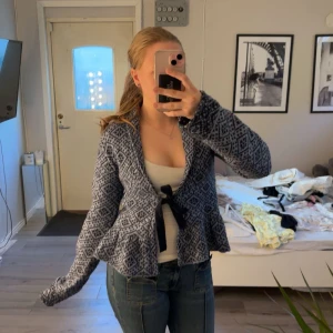 Mönstrad stickad cardigan från Nelly - Säljer en blå och vit stickad cardigan från Nelly med grafiskt mönster och knytband framtill. Koftan har lång ärm och volangdetalj nedtill, perfekt med ett enkelt linne under.🤍🍸