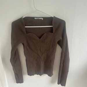 Brun ribbad topp med sweetheart-urringning från NA-KD - Säljer en brun långärmad topp från NA-KD med ribbad struktur och snygg sweetheart-urringning. Toppen har figurnära passform och markerade sömmar framtill för en trendig look. Bra skick.