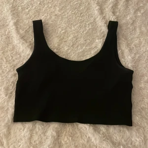 Svart croppad linnetopp - En enkel och svart ribbad croppad linnetopp med breda axelband och rundad halsringning. 