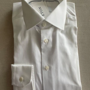 Vit skjorta från Eton - Klassisk vit skjorta från Eton i slim fit. Skjortan har lång ärm, knappar framtill och en stilren krage. Perfekt för dig som vill ha en tidlös och snygg look. Tillverkad i bomull för en skön känsla.