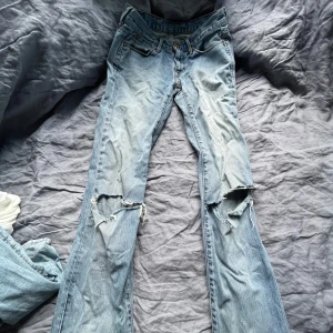 Ljusblå slitna bootcut jeans från Levis - Säljer ett par ljusblå bootcut jeans från Levis med slitningar och hål på båda knäna. Jeansen har fransiga benslut och klassiska fem fickor. Perfekta för en avslappnad och trendig look.