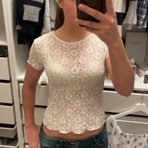 Vit spetsblus med kort ärm - Säljer en söt vit blus i spets med korta ärmar och rund hals. Blusen har ett blommigt spetsmönster och är lätt genomskinlig. Bara använd 2 gånger💕