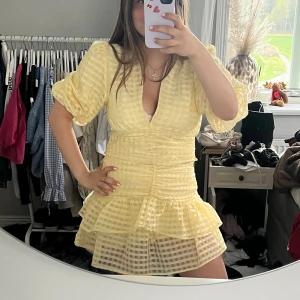 Gul volangklänning från Gina Tricot - Säljer en söt gult set från Gina Tricot med puffärmar och volanger. Settet har v-ringning, markerad midja och ett rutigt mönster i tyget. Perfekt för sommarens alla tillfällen!