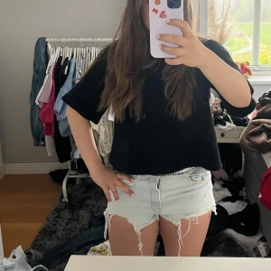 Ljusblå jeansshorts med fransar från TRF - Säljer ett par ljusblå jeansshorts från TRF med råa franskantsdetaljer. Shortsen har klassisk femficksdesign och är tillverkade i denim. Perfekta för varma dagar och har en avslappnad look.