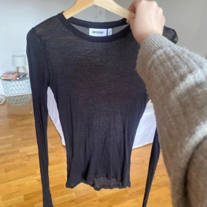 Svart tunn långärmad tröja från Weekday - Säljer en svart, tunn och långärmad tröja från Weekday. Tröjan har en rund halsringning och är gjord i ett lätt, transparent material som passar perfekt för lager-på-lager-stil.